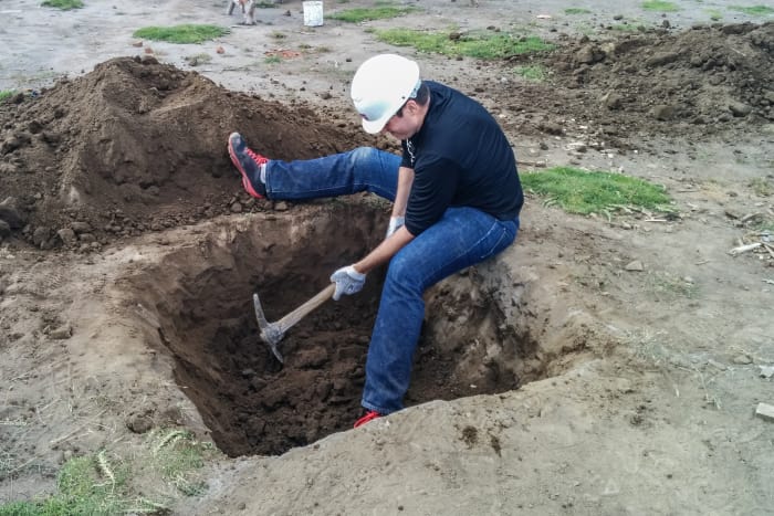Person with pickaxe digging foundation hole in ground
