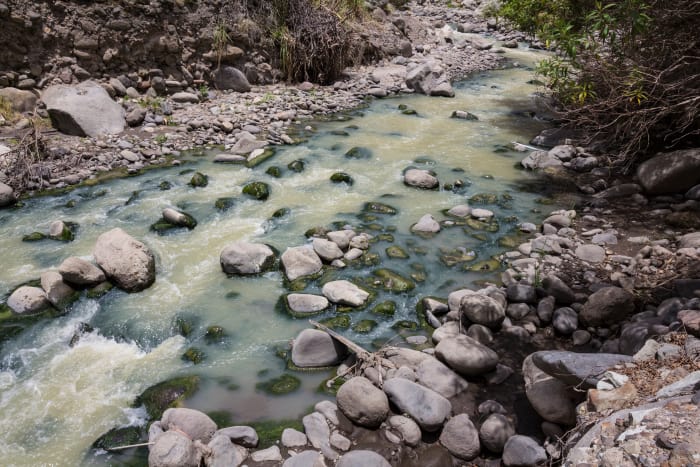 Green coloured water rushing over rocks at the bottom of the valley