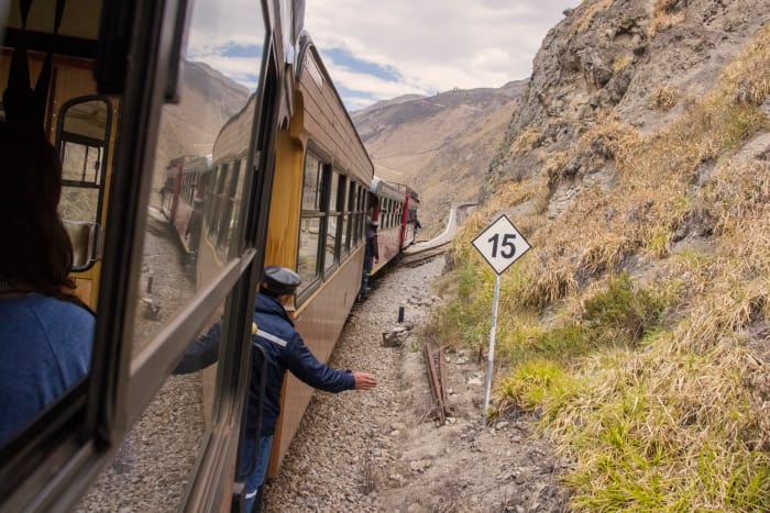 Train on tracks on side of a mountain, with a conductor signalling to continue on
