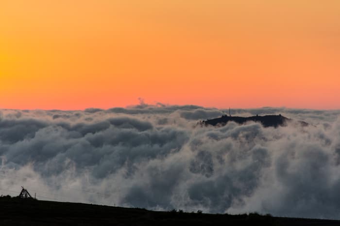 Silhouette of hill surrounded by clouds at sunset