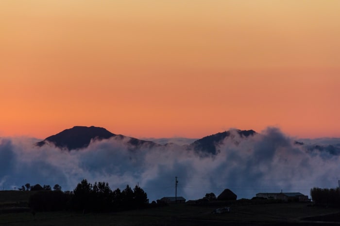 Silhouette of hill surrounded by clouds at sunset