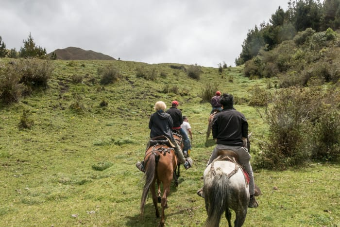 Group of people on horses start to climb up a clear green hill